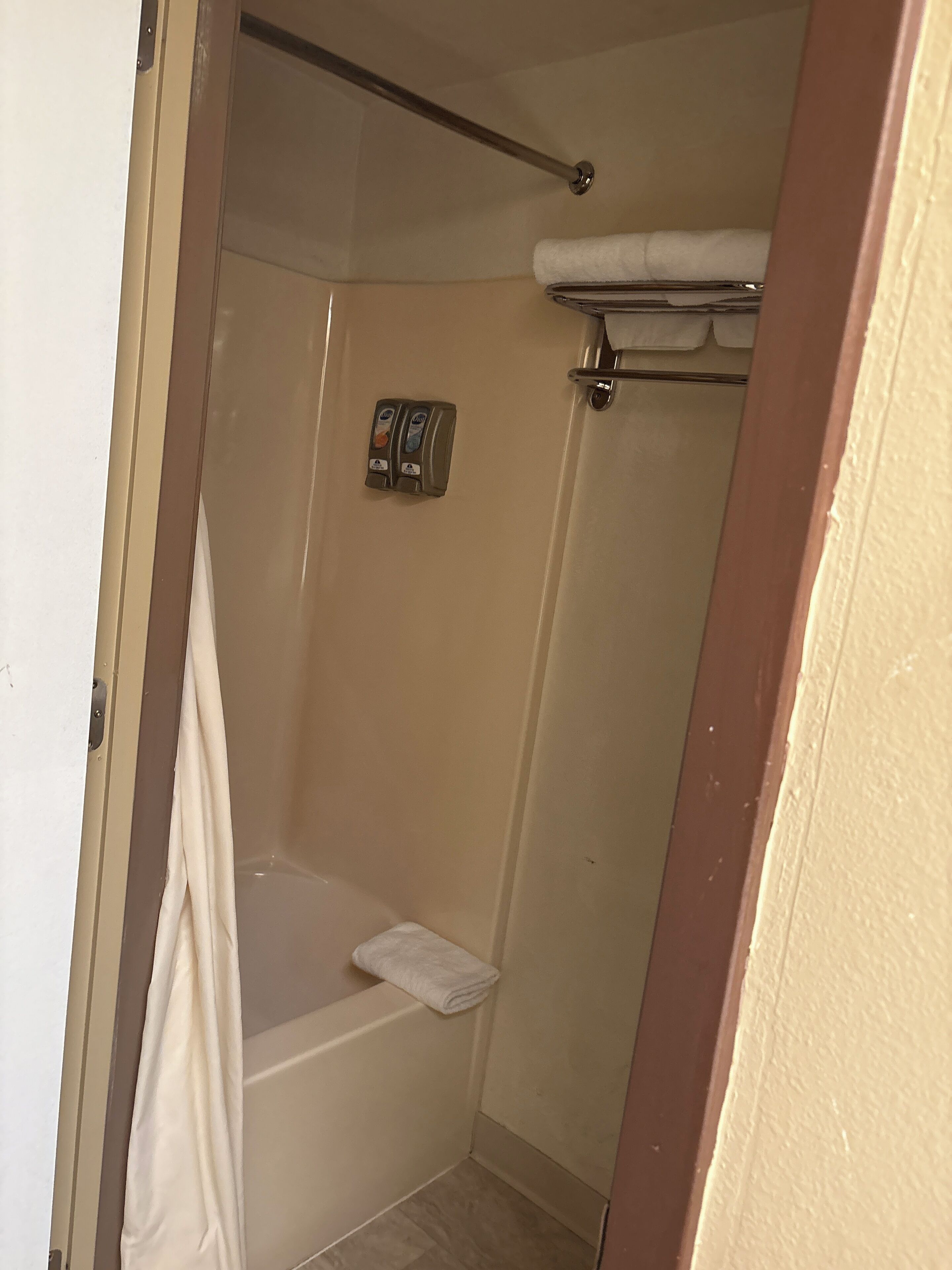 Un espacio de ducha pequeño y cerrado con bañera, un perchero para toallas y dispensador de jabón.