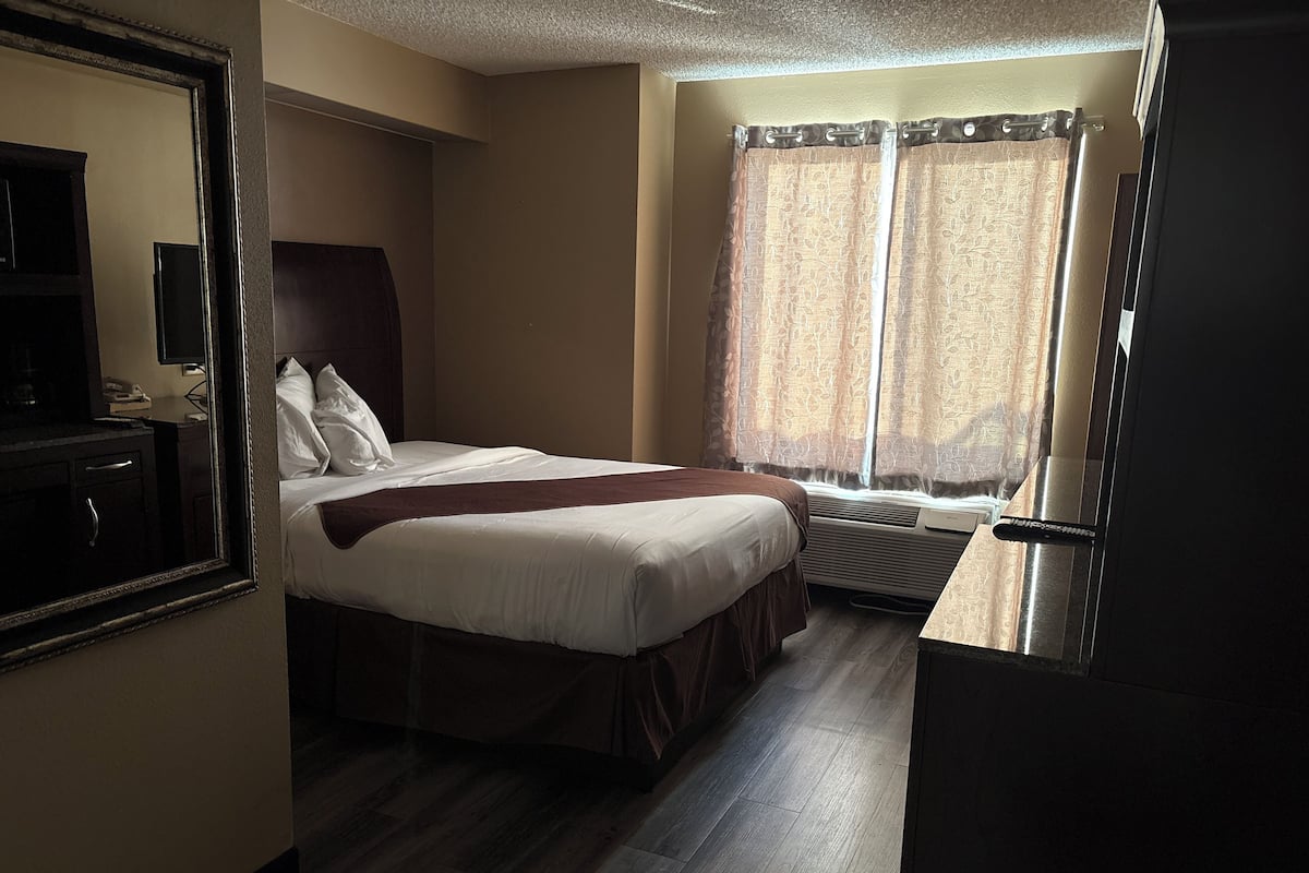 A hotel room with a bed, a desk, a mirror, and a window with curtains.