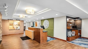 Un espace d’accueil avec un comptoir de réception en bois, un mur d’accent vert et un tapis à motifs.