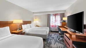 Une chambre d’hôtel avec deux lits, un bureau, une télévision et une fenêtre avec des rideaux.
