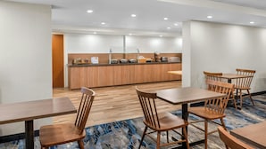 Une salle à manger d’hôtel avec des tables et des chaises en bois, une cuisine en arrière-plan et un tapis à motifs bleus.