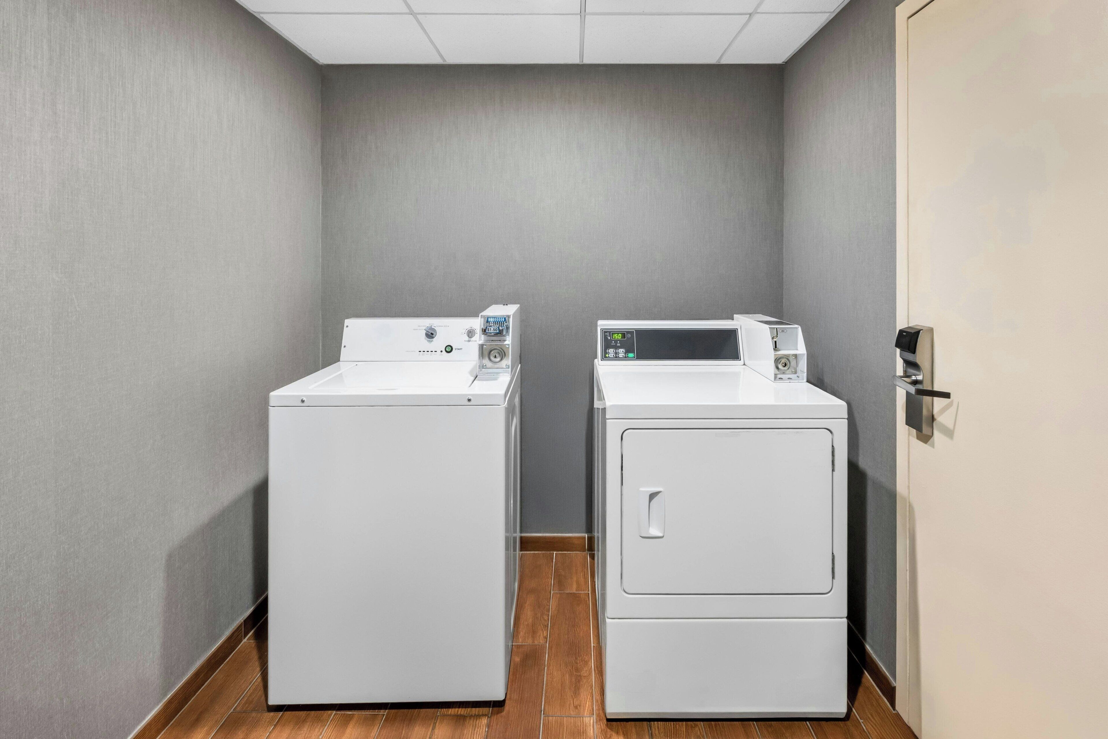 A laundry room with two white washing machines, a grey wall, and a wooden floor.