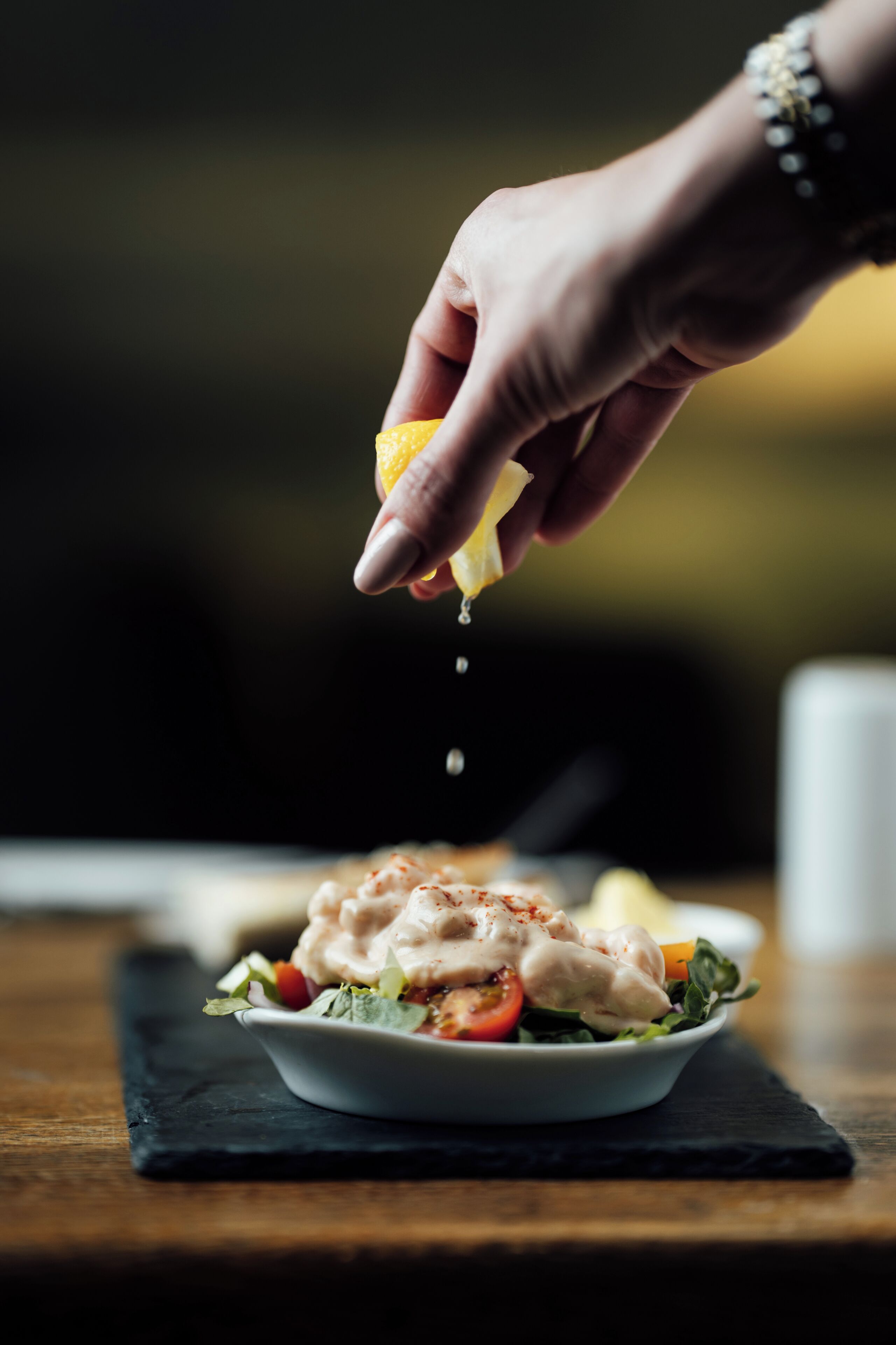 A hand squeezing a lemon over a salad.