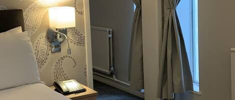 Una habitación de hotel con cama, lámpara de noche, teléfono, espejo y cortinas.