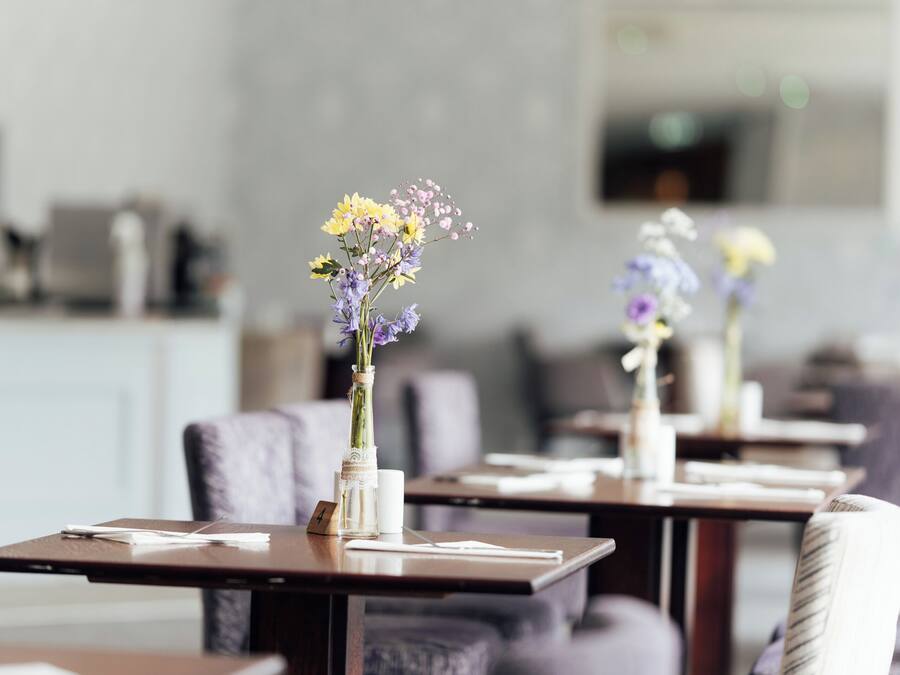 Un restaurante con mesas y sillas, algunas con jarrones de flores.