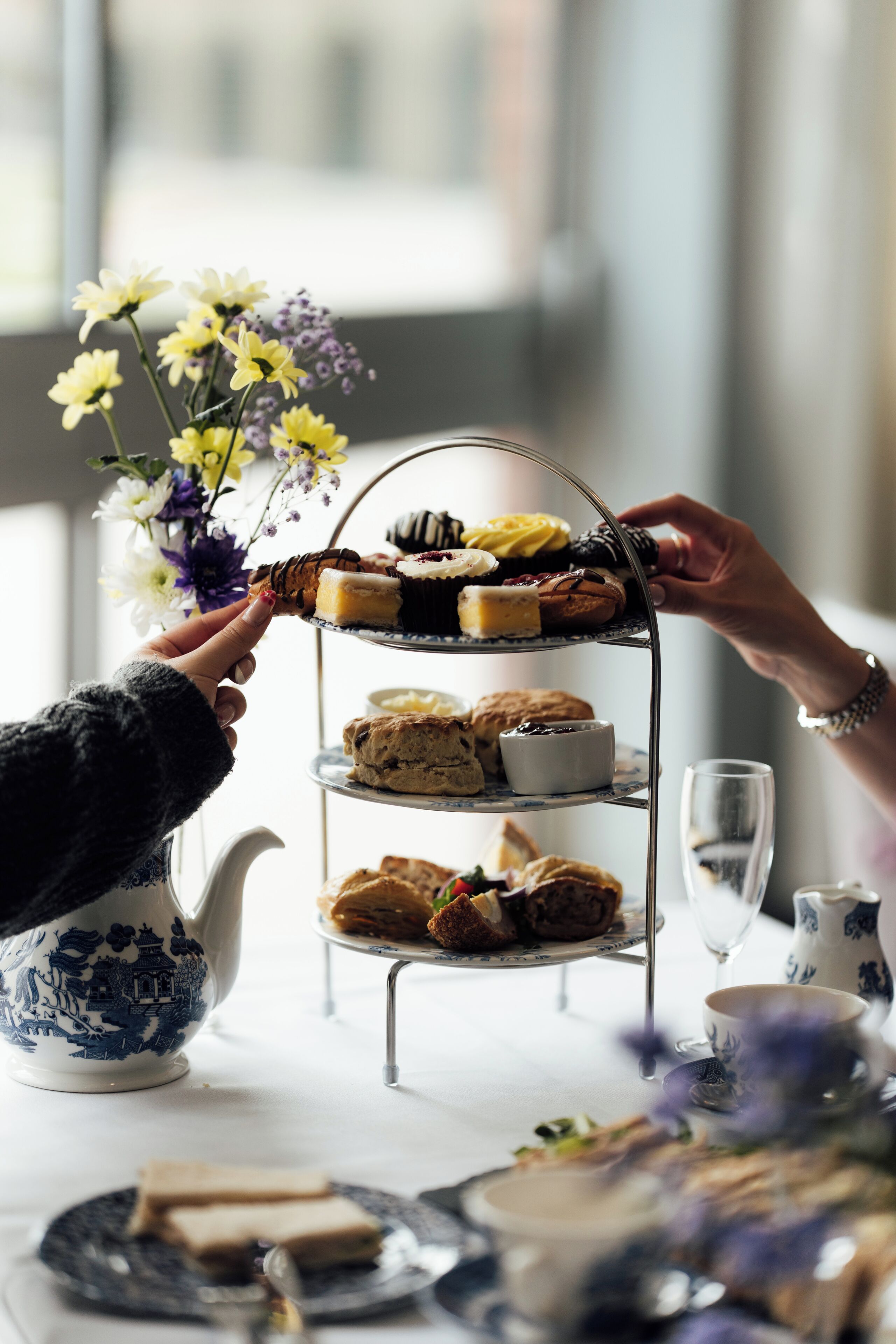 A tiered dessert stand with various pastries and a teapot on a table.