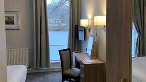 A hotel room with a bed, a desk with a computer, a chair, a window with curtains, and a radiator. - Corus St James Hotel Grimsby (Grimsby)
