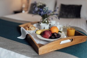 A breakfast tray with fruits, a glass of orange juice, and a white teapot on a bed with a blue blanket and a vase of flowers. - Corus St James Hotel Grimsby (Grimsby)