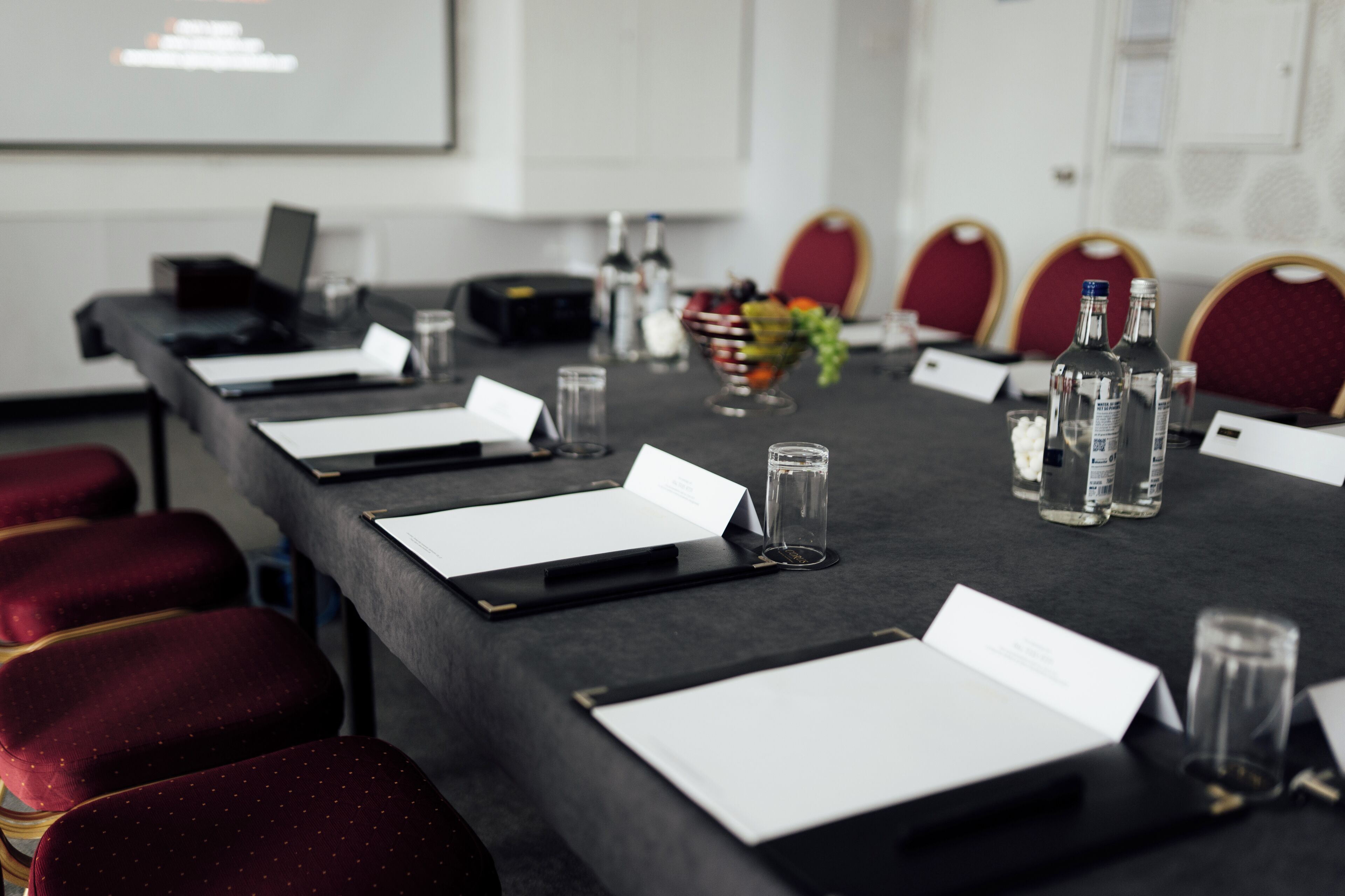 Ein Konferenzraum mit langem Tisch, Stühlen, einer Projektionsleinwand und einer Obstschale.