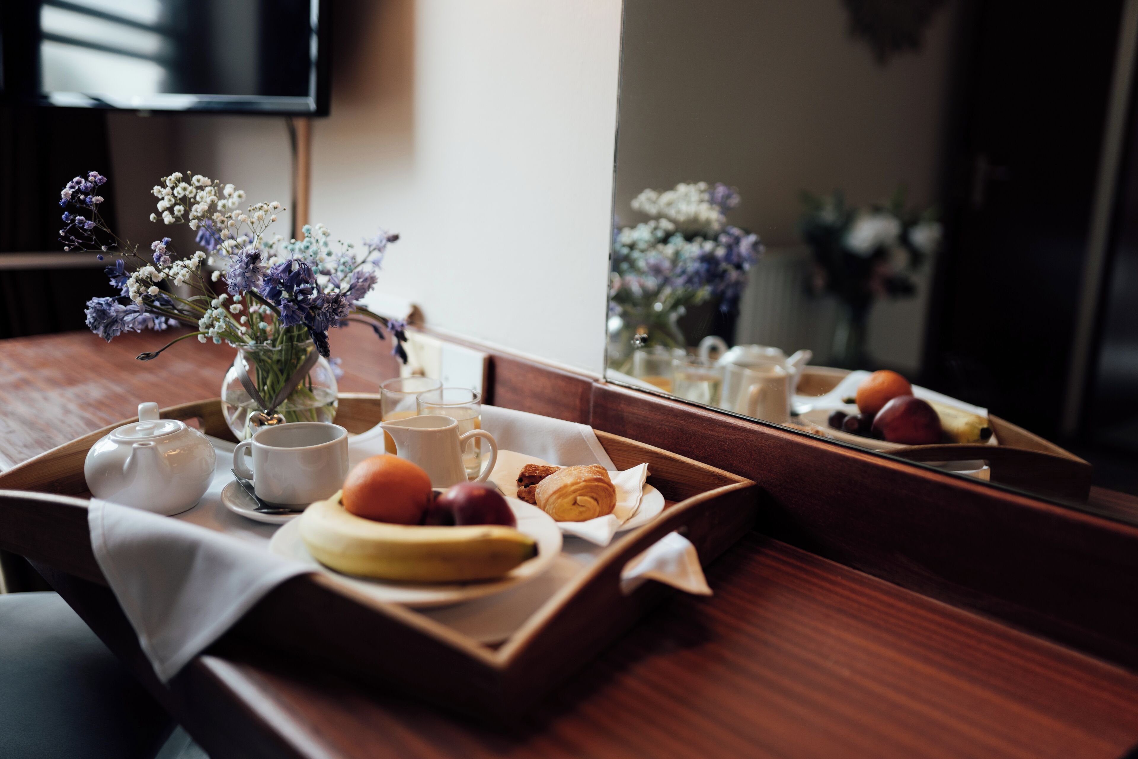 Un plateau de petit-déjeuner avec des fruits, un croissant et un vase de fleurs sur une table en bois.