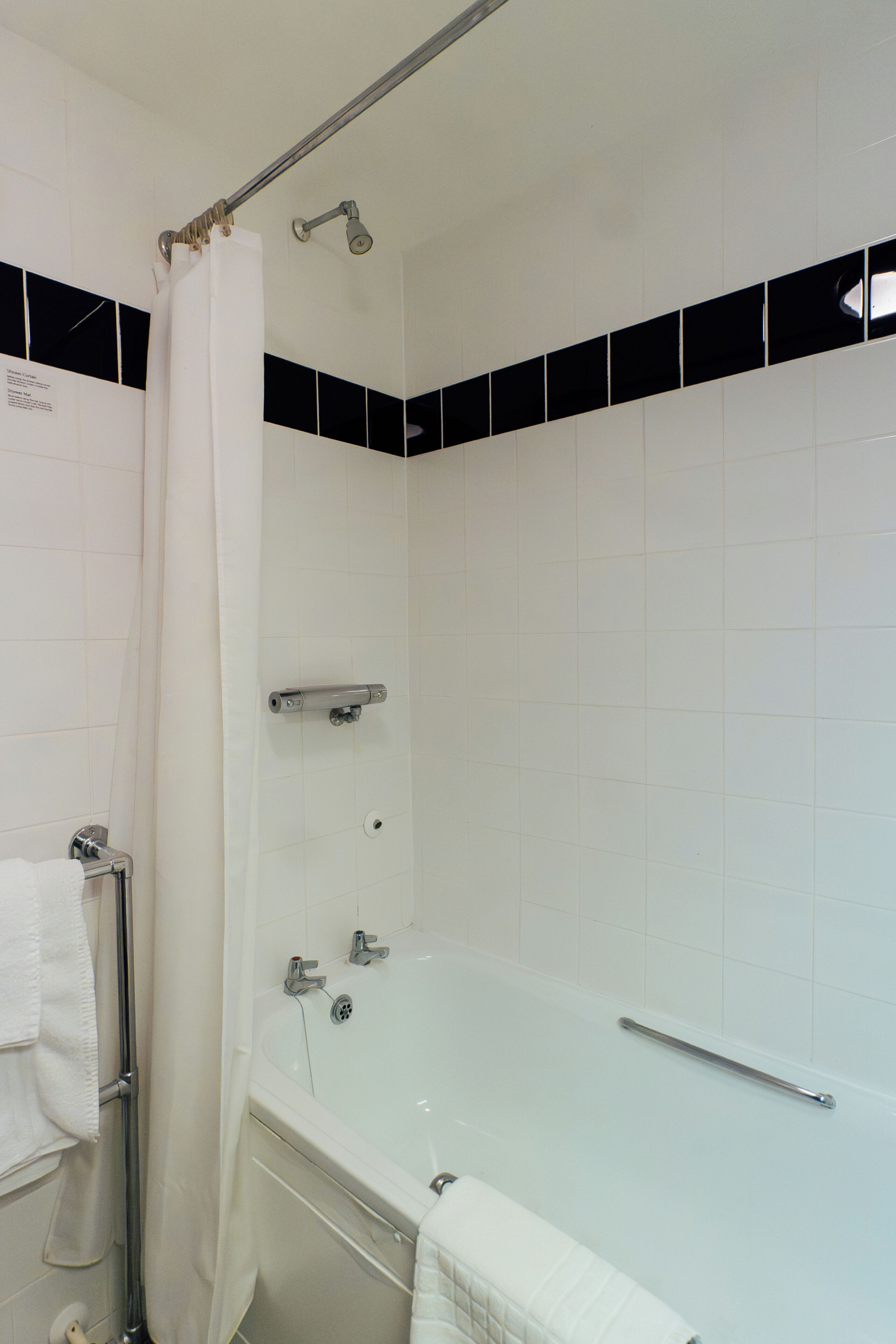 Een badkamer met een bad, douchegordijn en een handgreep.