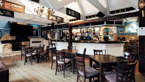 A bar area with wooden furniture, a counter with a beverage display, and a sign indicating live music. - Corus St James Hotel Grimsby (Grimsby)