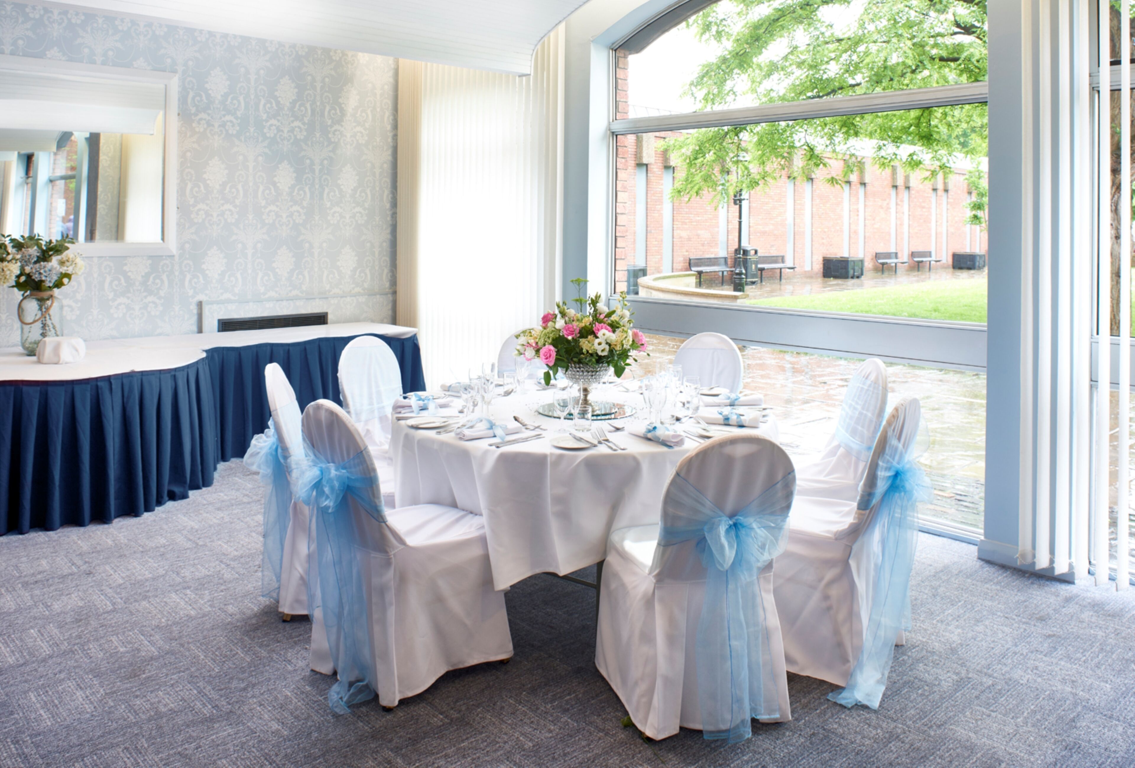 A conference room with a round table set for a meeting, large windows, and a view of the outdoors.