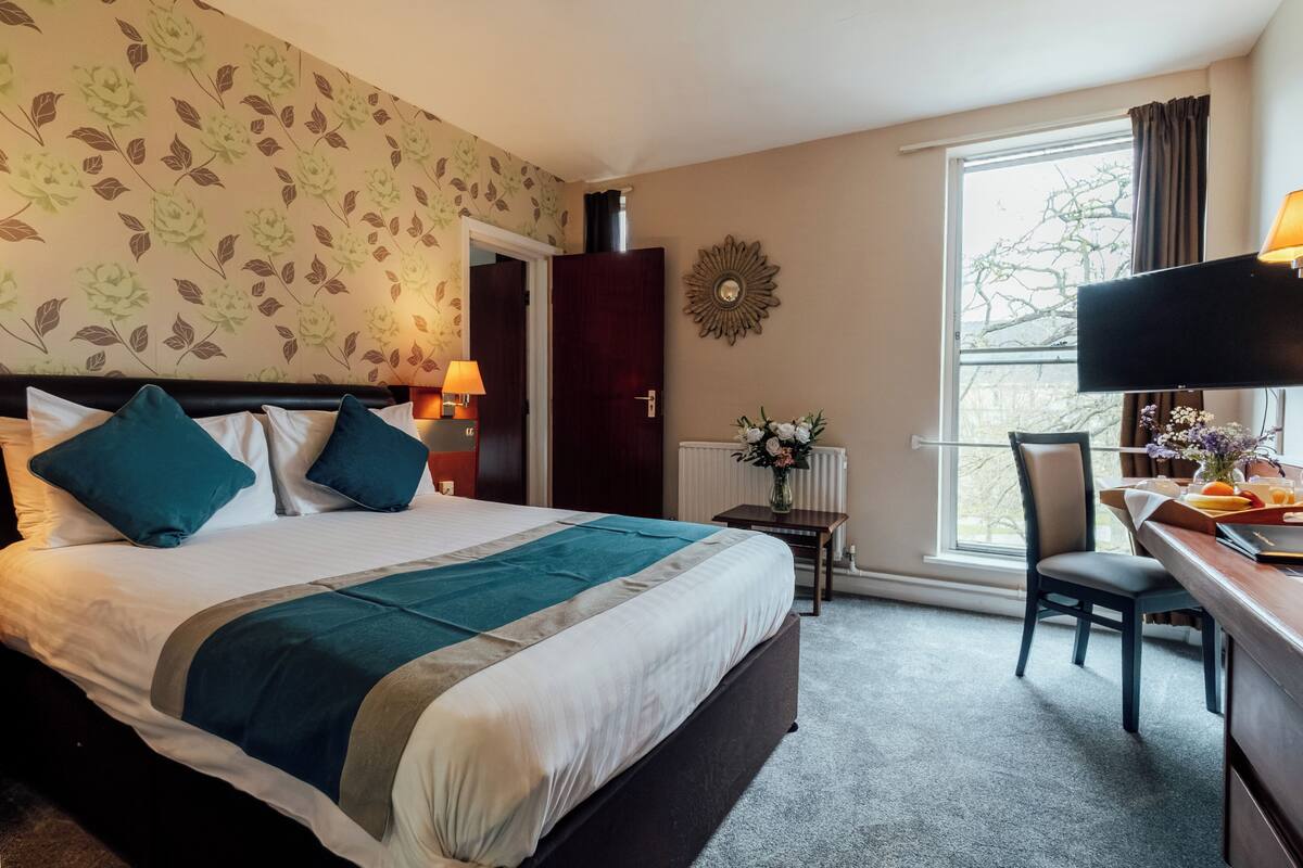 Habitación de hotel con cama, escritorio, silla, televisor, ventana y puerta.