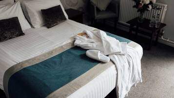 A neatly made bed with a teal and white bedspread, a white bathrobe, and slippers on it.