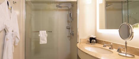 Une salle de bain moderne dotée d’une douche à parois de verre, d’un lavabo avec un miroir et d’un porte-serviettes avec des peignoirs.