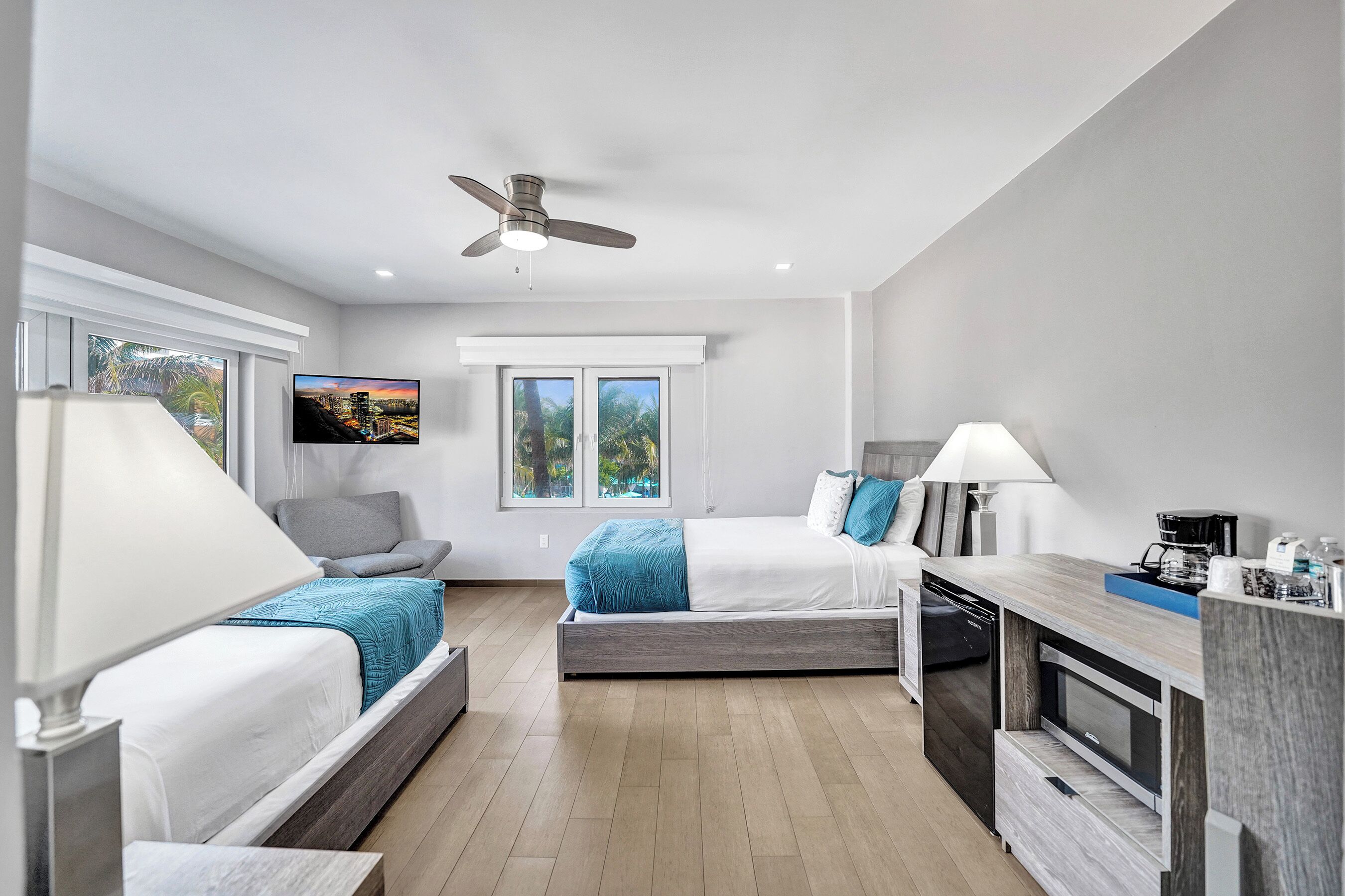 A modern hotel room with two beds, a dining area, and a ceiling fan.