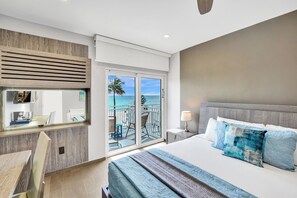 Quarto com uma cama grande, uma escrivaninha e uma varanda com vista para o mar.