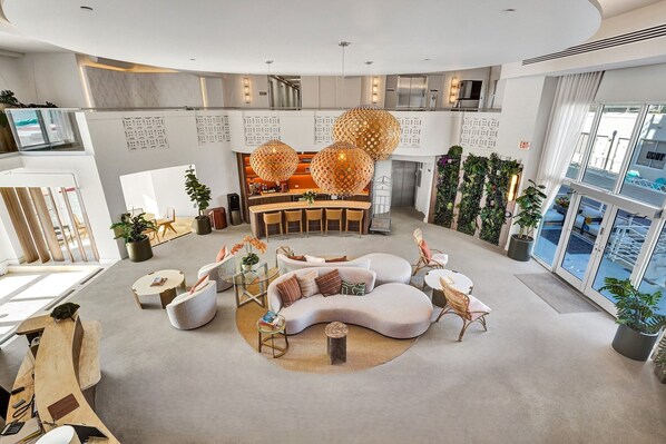 A modern hotel lobby with a curved sofa, a reception desk, and large windows offering a view of the city. - Hotel Sheldon (Hollywood)