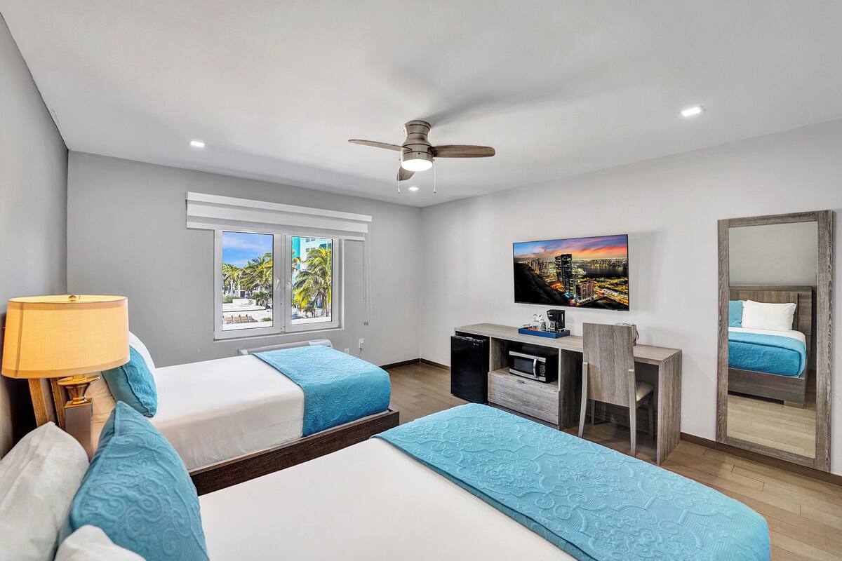 A hotel room with two beds, a desk, a TV, and a ceiling fan.