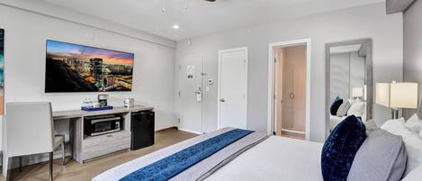 Una habitación de hotel moderna con una cama grande, un escritorio con televisión de pantalla plana, un ventilador de techo y un cuadro de un paisaje urbano en la pared.
