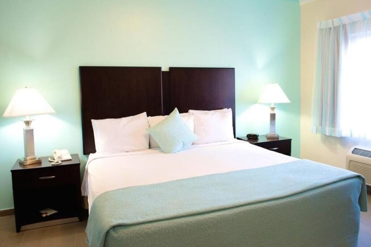 A neatly made bed with white linens and a dark headboard, two bedside tables with lamps, and a window with curtains.