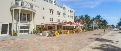 A hotel with a white facade, a balcony, and outdoor seating with umbrellas.