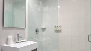 A modern bathroom with a glass-enclosed shower, a white sink with a wooden vanity, and a large mirror.