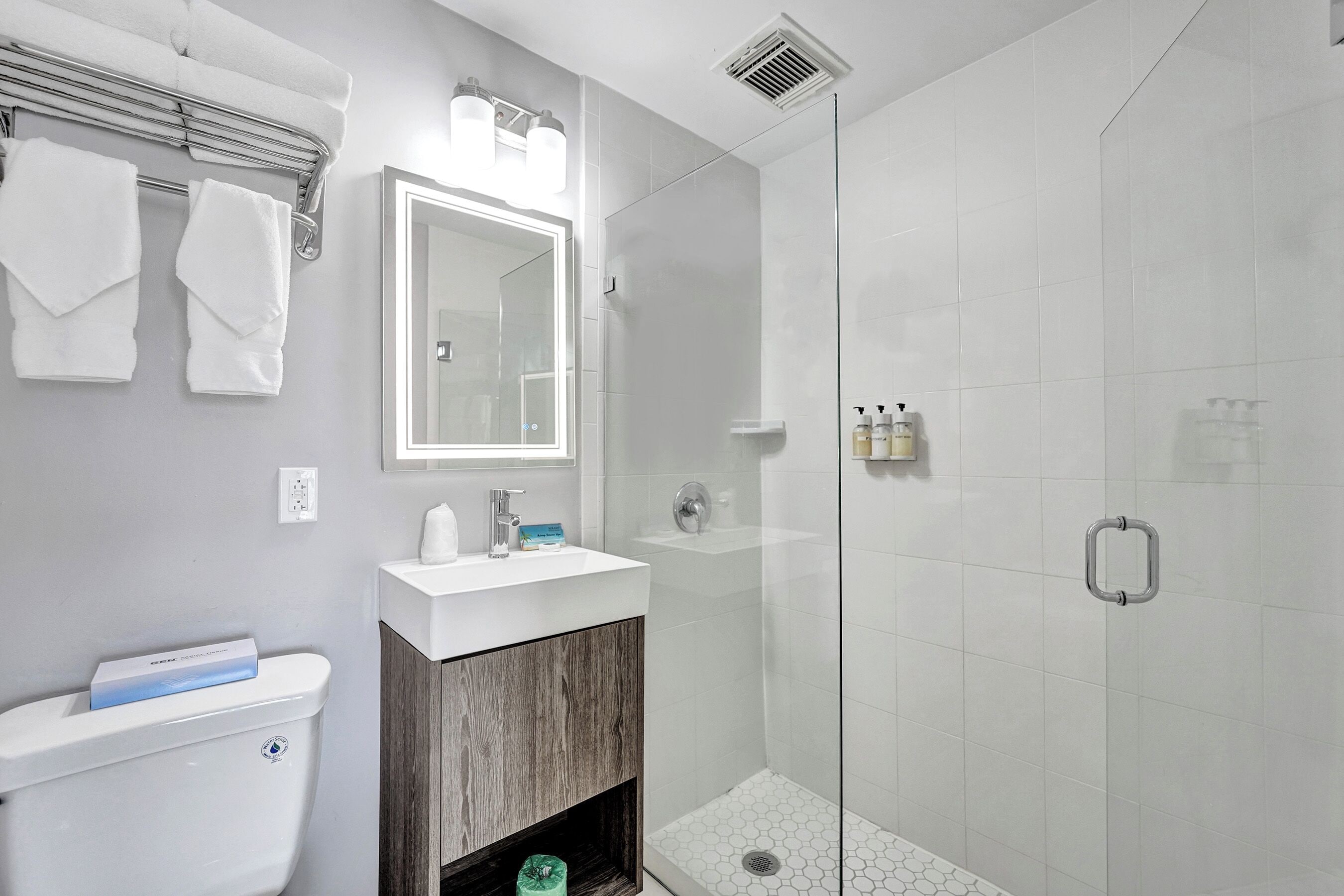 A modern bathroom with a toilet, sink, mirror, and glass shower enclosure.