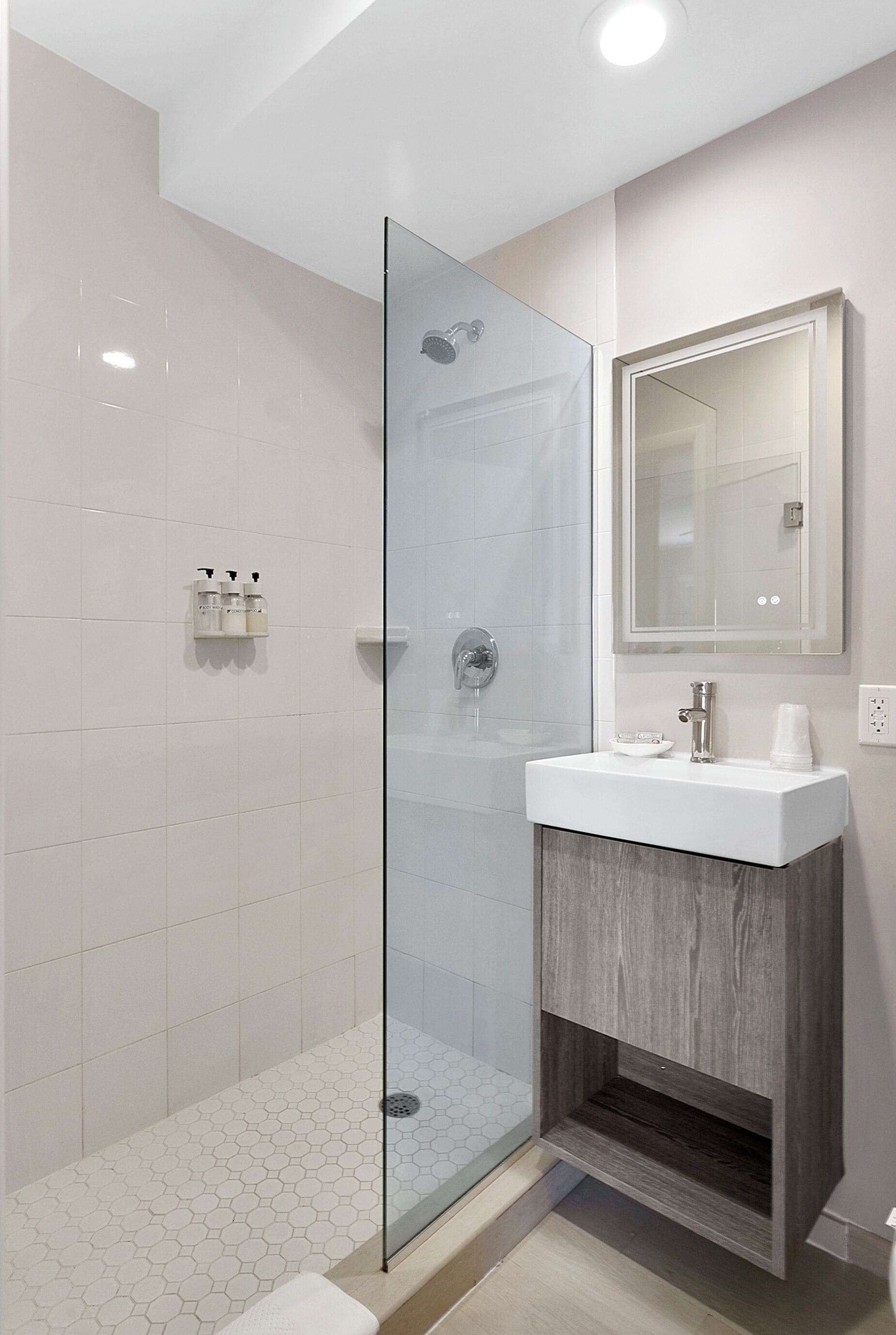 A modern bathroom with a glass shower enclosure, a white sink with a wooden cabinet, and a mirror above the sink.