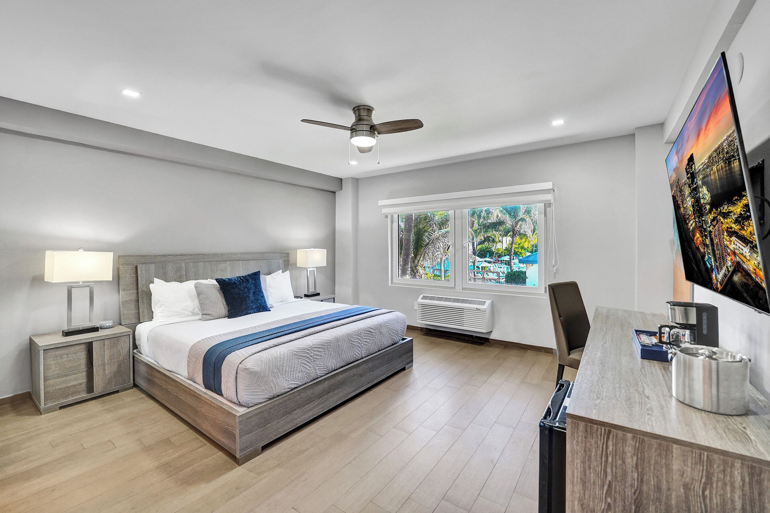A modern bedroom with a bed, bedside tables, a desk, and a ceiling fan.