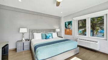 A modern bedroom with a bed, bedside tables, a ceiling fan, and a window with a view of palm trees.
