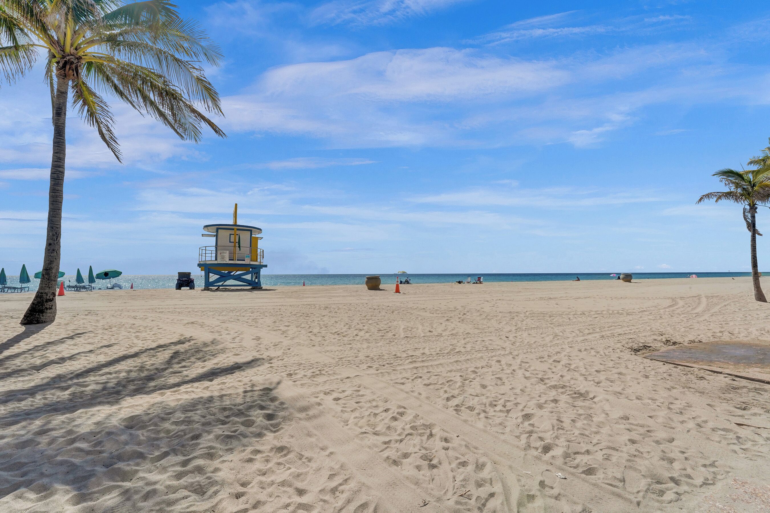 Une plage avec une tour de surveillance pour les sauveteurs, des palmiers et des parasols.