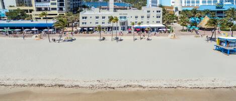 Un hotel frente a la playa con piscina, palmeras y vista al océano.