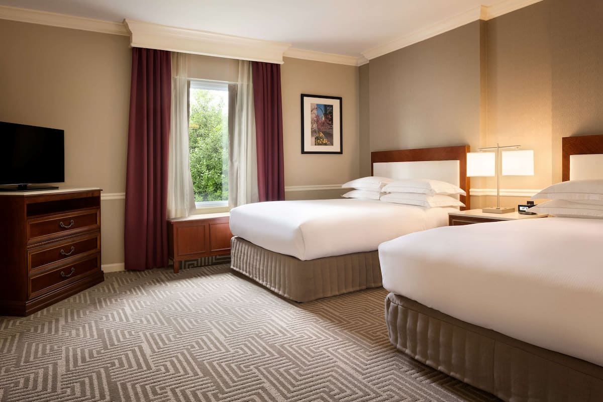 A hotel room with two beds, a TV, a dresser, and a window with curtains.