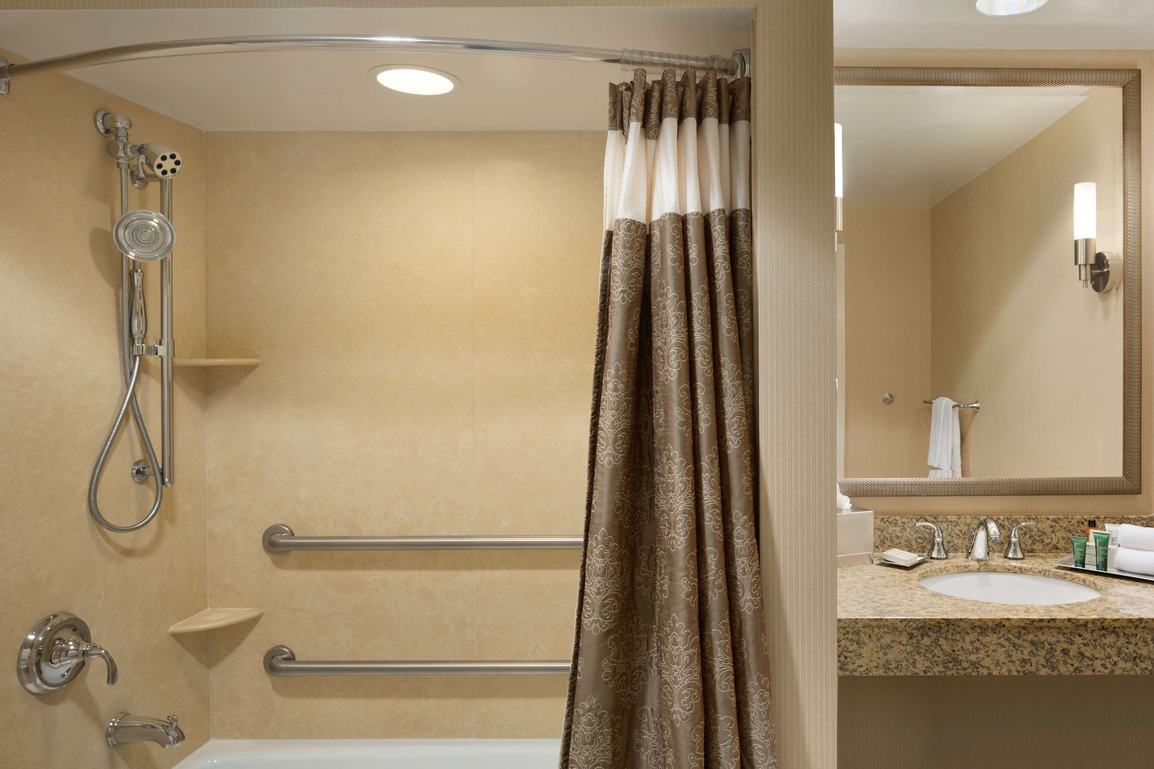 A bathroom with a shower, grab bars, a sink, and a mirror.