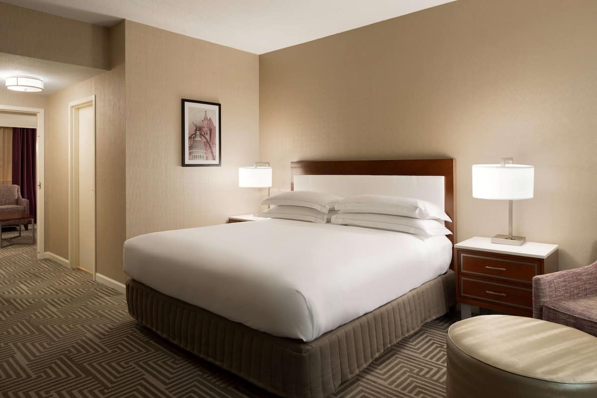A hotel room with a large bed, two bedside tables, a chair, and a carpeted floor.