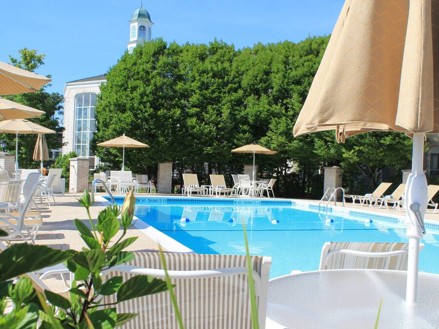 Zona de piscina con sillones y sombrillas, una piscina azul cristalina y un edificio con cúpula al fondo.