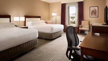 A hotel room with two beds, a desk, a chair, a lamp, and a television.