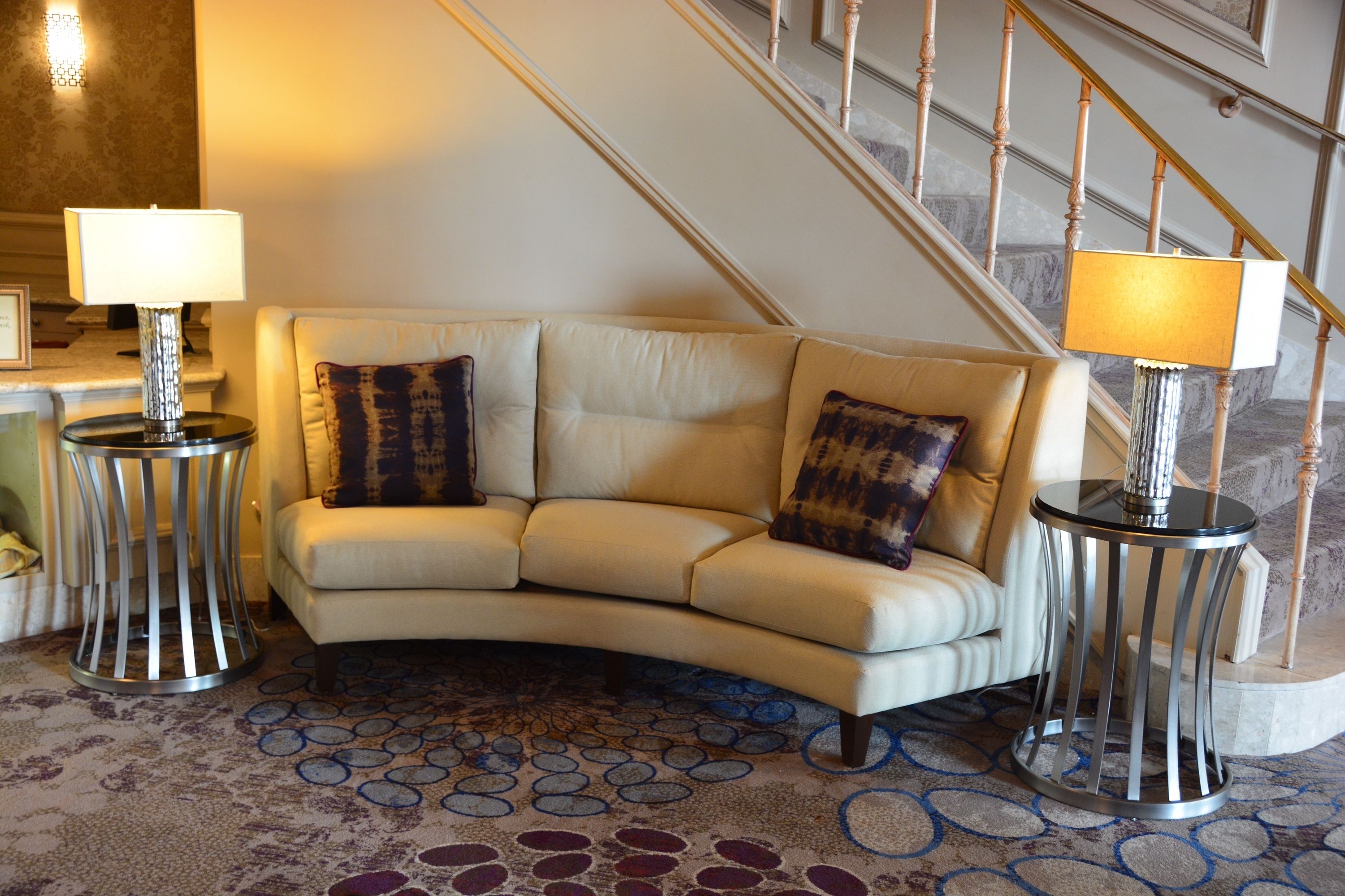 A living room with a beige sofa, two side tables with lamps, a patterned rug, and a staircase in the background.