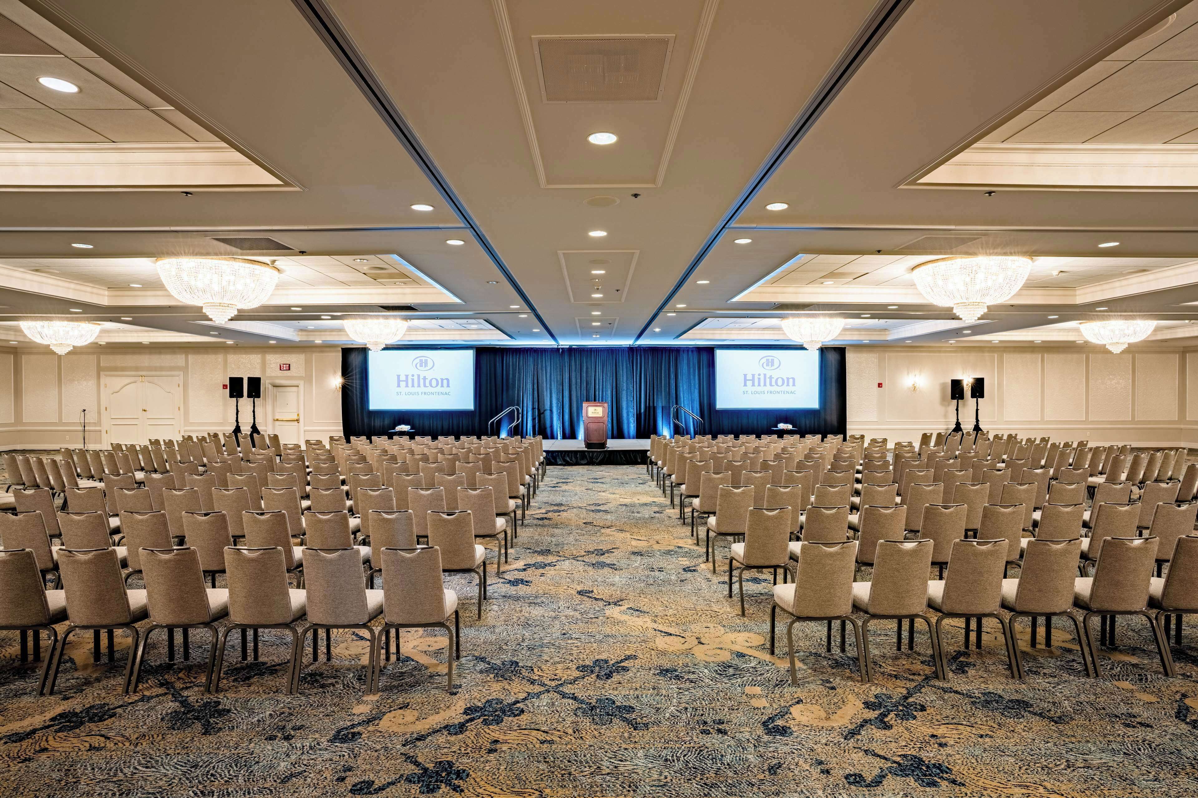 A conference room with rows of chairs facing a stage with a blue curtain and a podium.