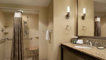 A hotel bathroom with a shower, a sink, a mirror, and a towel rack.