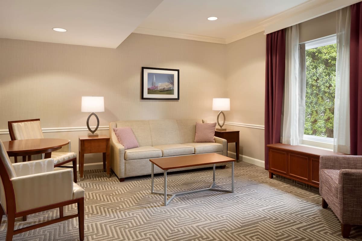 A hotel room with a sofa, two armchairs, a coffee table, and a window with curtains.