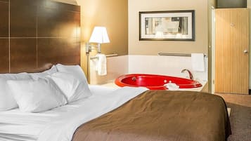 A hotel room with a large bed, a red bathtub, a wall-mounted mirror, and a wooden door.