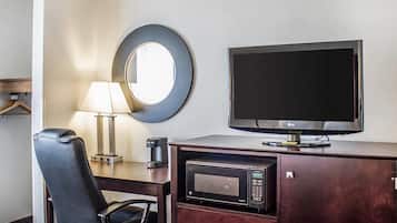 A hotel room with a flat-screen TV, a microwave, a desk with a chair, and a round mirror on the wall.
