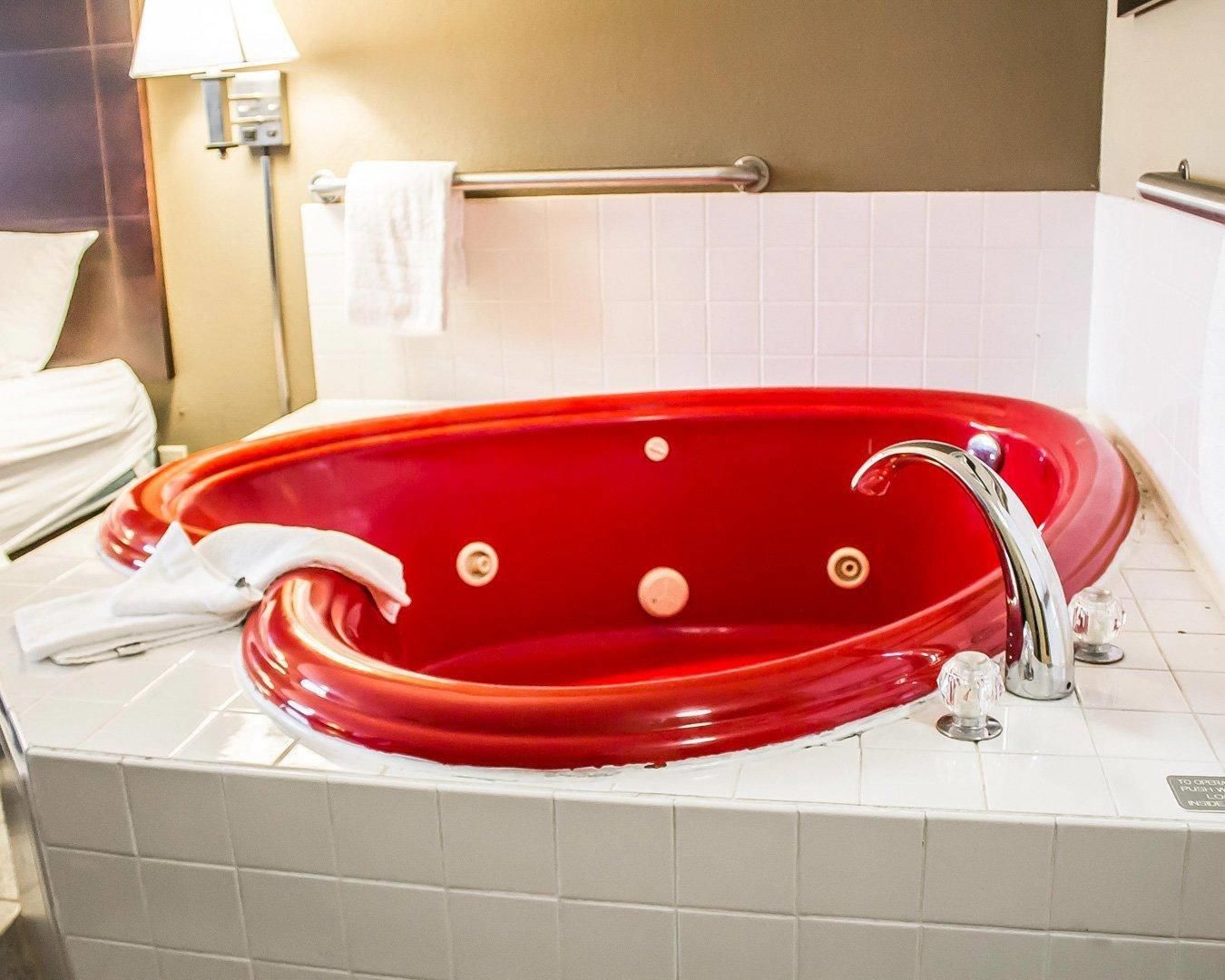 A red bathtub in a bathroom with white tiles, a towel rack, and a lamp.