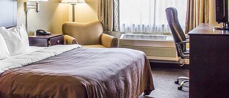 A hotel room with a large bed, two bedside lamps, a chair, a desk with a computer, and a window with curtains.