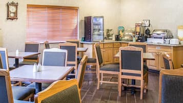 A restaurant with wooden tables and chairs, a refrigerator, and a coffee machine.