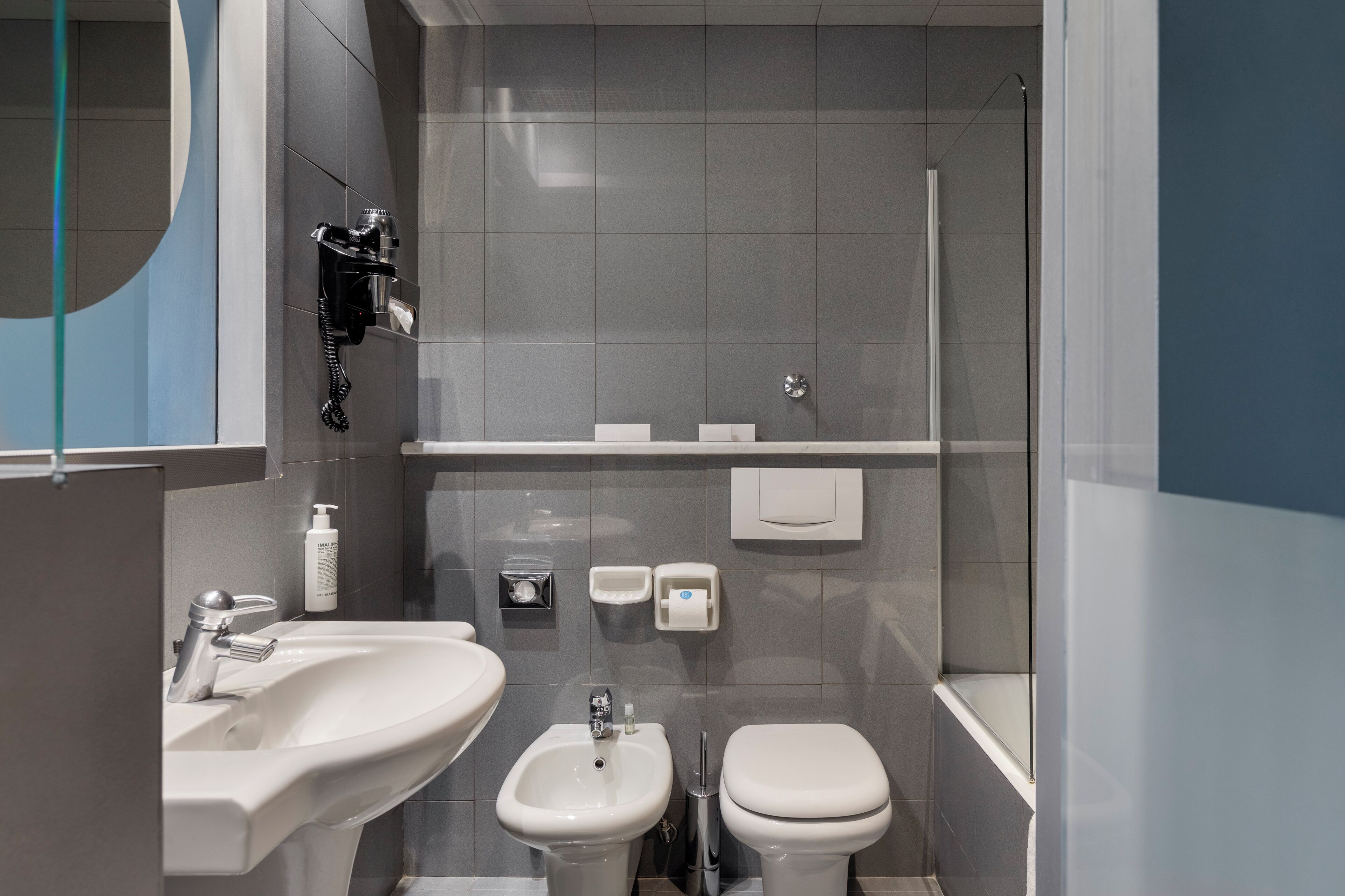 A modern bathroom with a sink, bidet, toilet, and a glass shower enclosure.