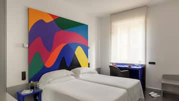 A hotel room with two beds, a desk, a chair, a colorful abstract painting, and a window with blinds.